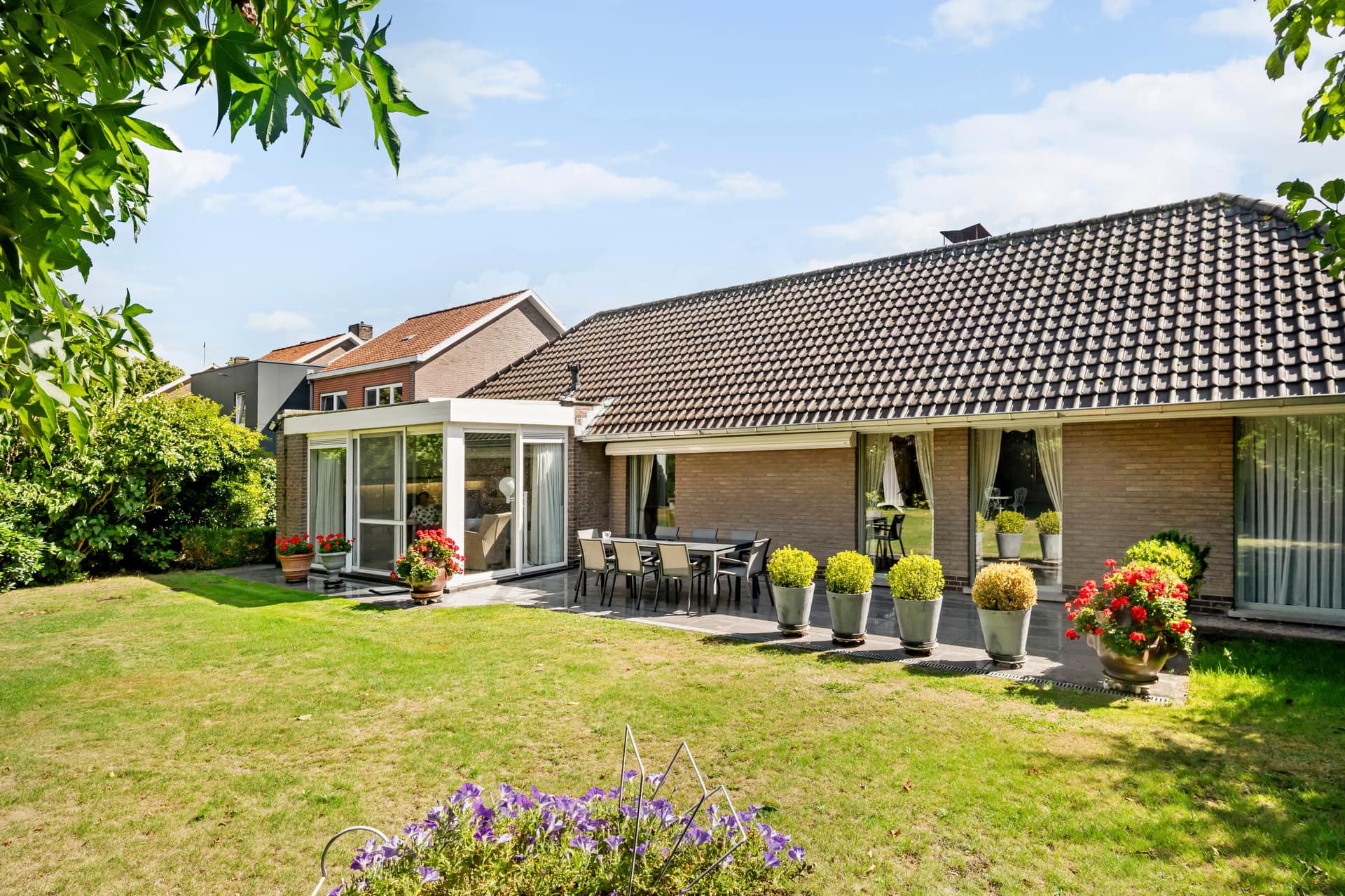 Achtergevel van de villa met veranda, terras en zonnige tuin